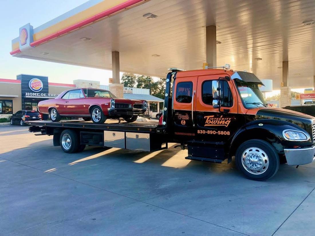 Integrity Towing flatbed hauling a classic car at a Kerrville gas station